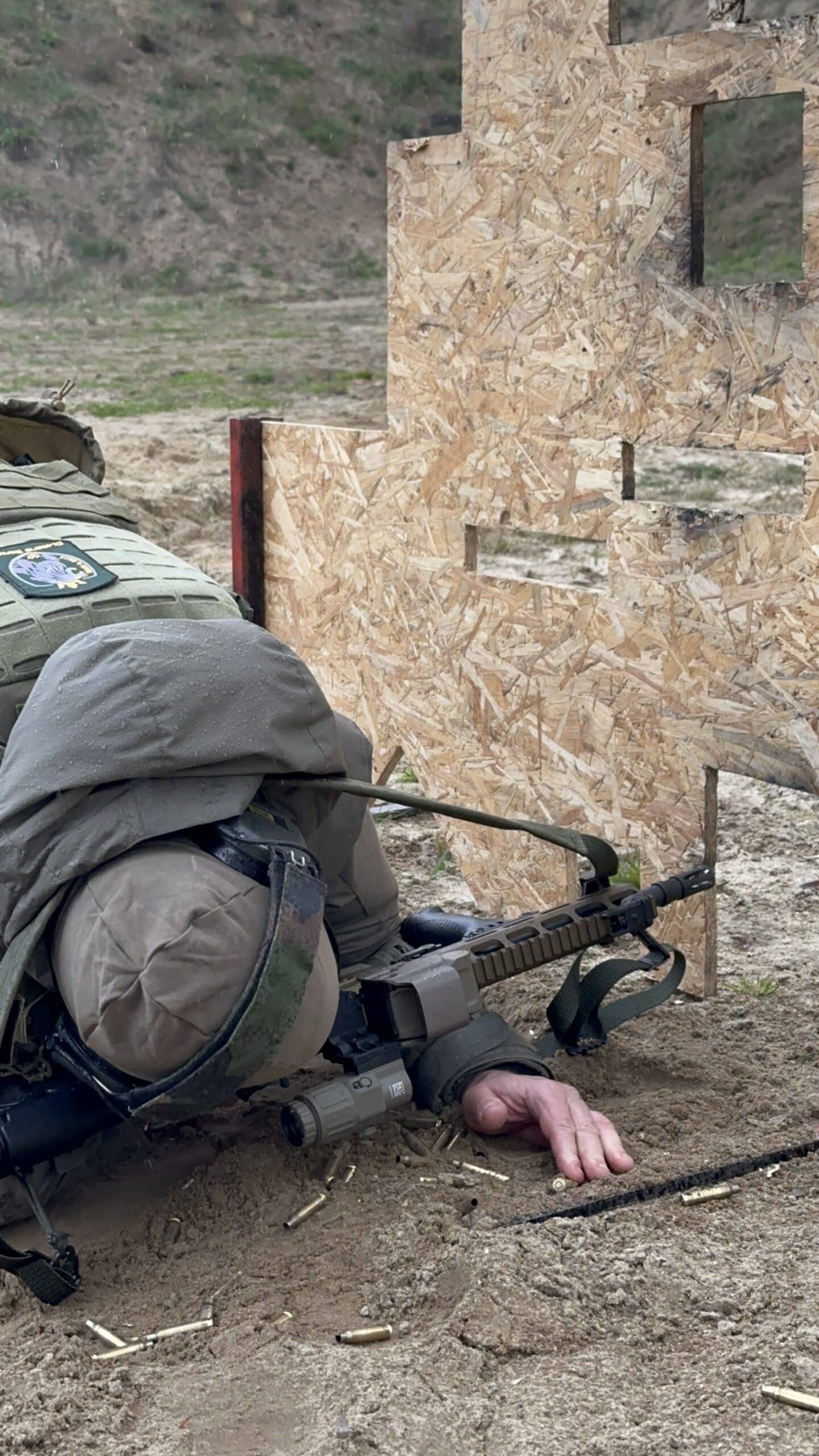 Liegender Schütze zielt mit einem Gewehr neben einer hölzernen Deckung.