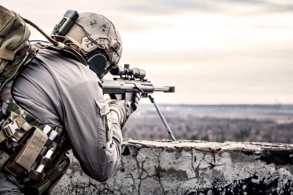 Schütze zielt mit einem Gewehr und Zielfernrohr über eine Mauer in die Ferne.
